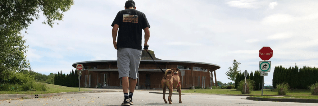 a man walking a dog towards the Musqueam Cultural Centre